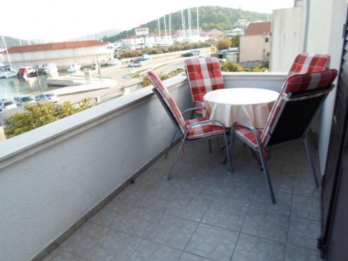 Un balcón con mesa y sillas, vista a un puerto deportivo y un edificio al fondo.