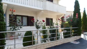 A two-story building with balconies, a paved driveway, and potted plants.