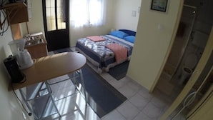 Una habitación pequeña y funcional con cama, escritorio y kitchenette.