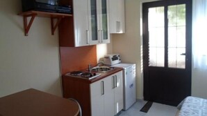 Una habitación compacta con kitchenette, una pequeña mesa, una cama y un ventanal con cortinas.