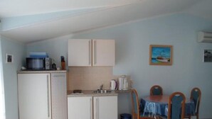 A compact kitchen with white cabinets, a microwave, and a coffee maker. There is a dining table with four chairs and a small trash bin. - Apartment in Rogoznica with Seaview, Balcony, Air condition, WIFI (5153-3) (Rogoznica)