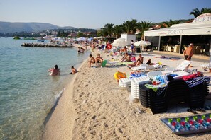 A beach with clear water, umbrellas, and lounge chairs. There are people swimming and relaxing on the sand.