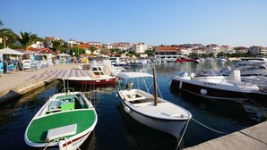 A marina with several boats docked, a sandy shore with umbrellas, and buildings in the background. - Apartment in Okrug Gornji with Terrace, Air condition, WIFI, Washing machine (5157-1) (Okrug Gornji)