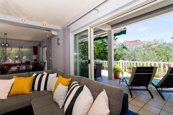 A modern living room with a grey sofa, yellow and white cushions, and a dining area with a kitchen in the background.