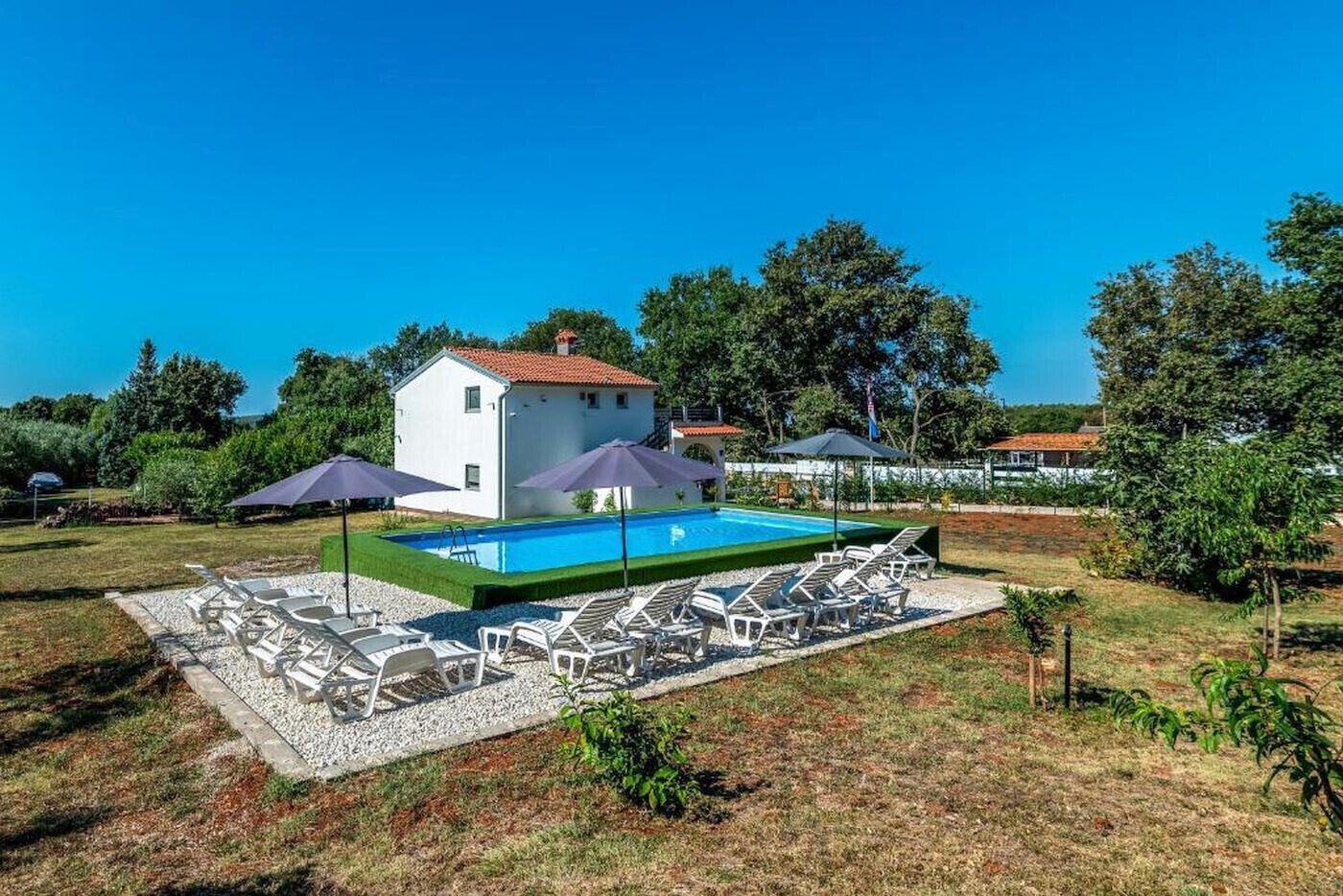 Una casa con piscina, rodeada de sillones de descanso y sombrillas.