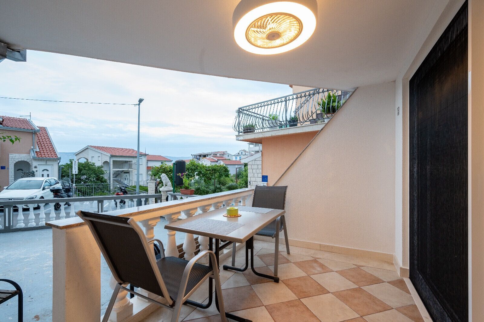 A balcony with a table and chairs, a railing, and a view of the street and buildings.
