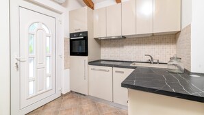 Een keuken met witte kastjes, een zwarte oven, een spoelbak en een marmeren aanrecht.