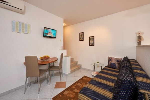 A compact living space with a sofa, a dining table with chairs, a small TV, and a staircase.