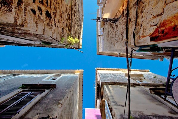 A narrow street between buildings with visible balconies and a clear blue sky. - Studio apartment in Mastrinka with Loggia, Air condition, WIFI, Washing machine (5159-1) (Mastrinka)