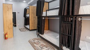 Een kamer met stapelbedden, een houten deur, een brandblusser en een kamerkleed met een patroon.