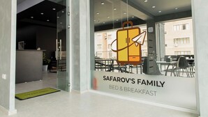 Een hotel receptie met een glazen deur die leidt naar een eetgedeelte. Het bordje luidt: Safarov's Family Bed & Breakfast.