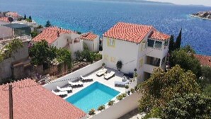 A coastal hotel with a swimming pool, terracotta-roofed buildings, and a view of the sea.