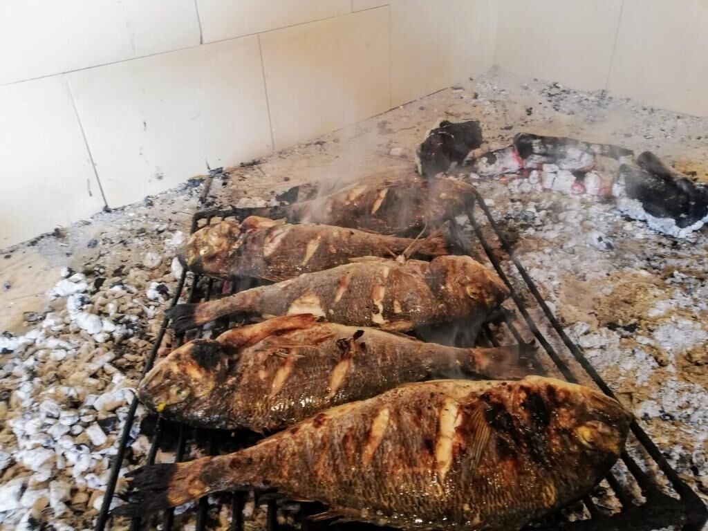 Several fish being grilled on a charcoal grill.