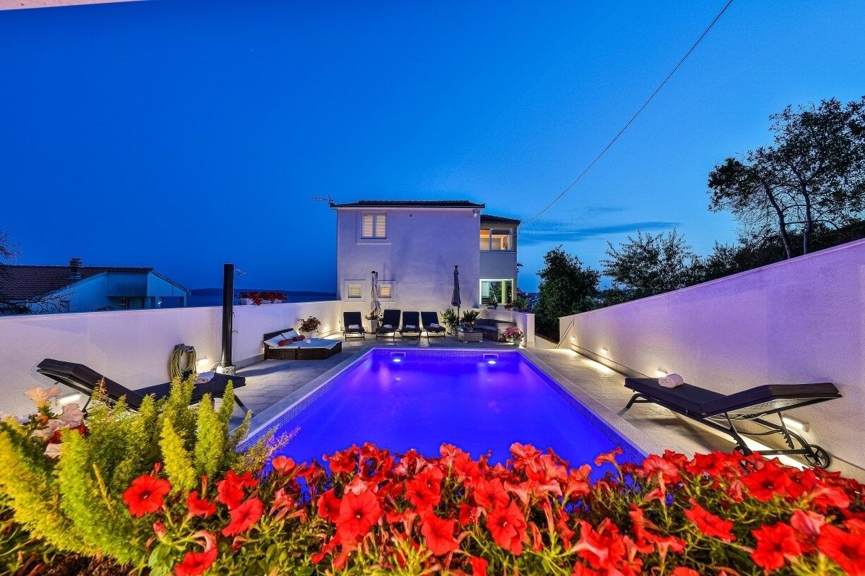 A swimming pool with lounge chairs, a building in the background, and red flowers in the foreground.
