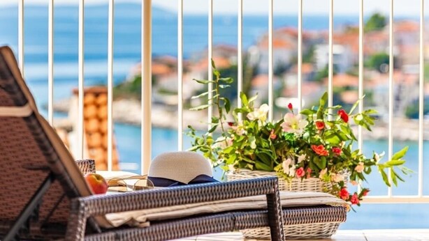 A balcony with wicker furniture, a wicker basket with flowers, and a view of a coastal town. - Apartment in Okrug Gornji with Seaview, Terrace, Air condition, WIFI (5160-2) (Okrug Gornji)