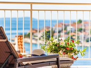 A balcony with wicker furniture, a wicker basket with flowers, and a view of a coastal town. - Apartment in Okrug Gornji with Seaview, Terrace, Air condition, WIFI (5160-2) (Okrug Gornji)