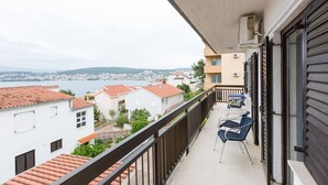 A balcony with a view of a lake and buildings, two chairs, and a railing.