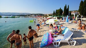 A crowded beach with people sunbathing and swimming, umbrellas, and beach chairs.