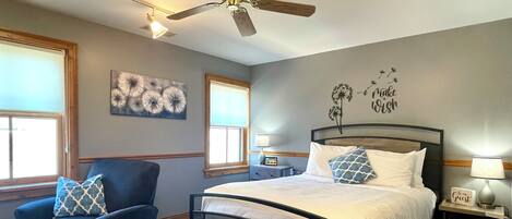 A bedroom with a bed, a chair, a ceiling fan, and a nightstand with a lamp.