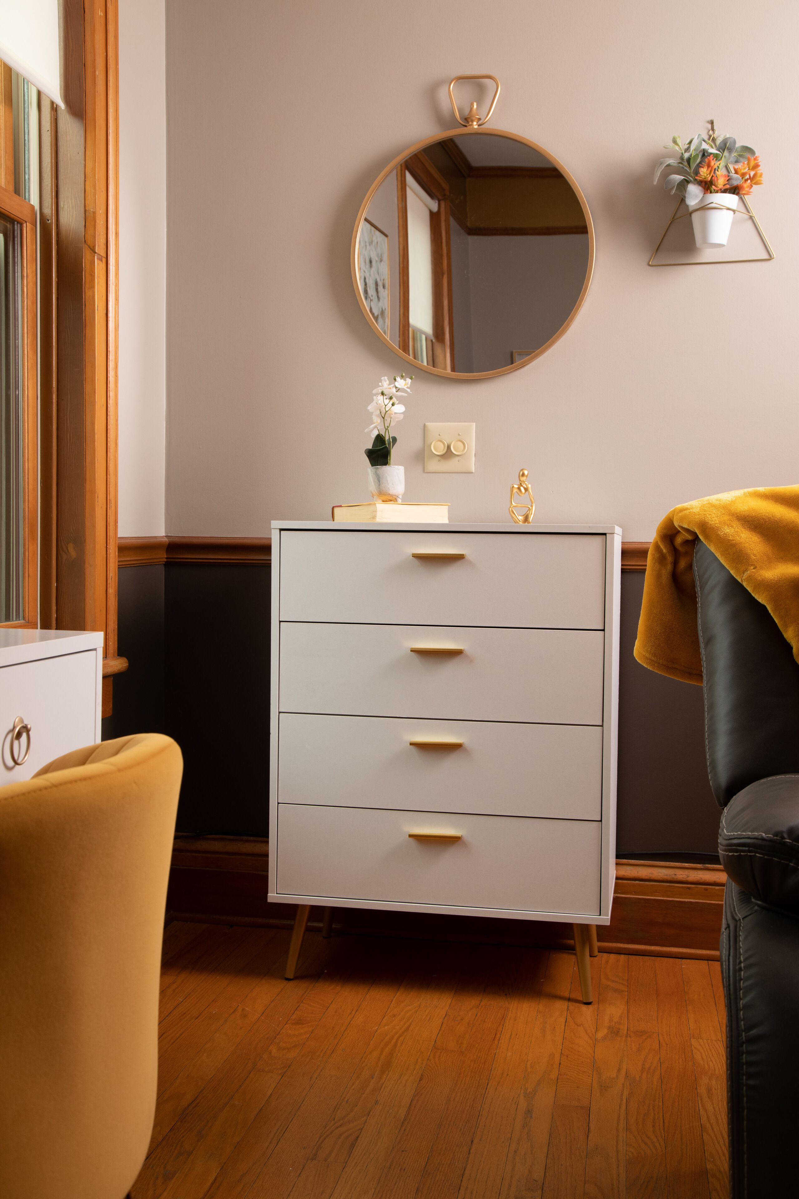 A room with a white dresser, a round mirror, a small potted plant, and a yellow chair.