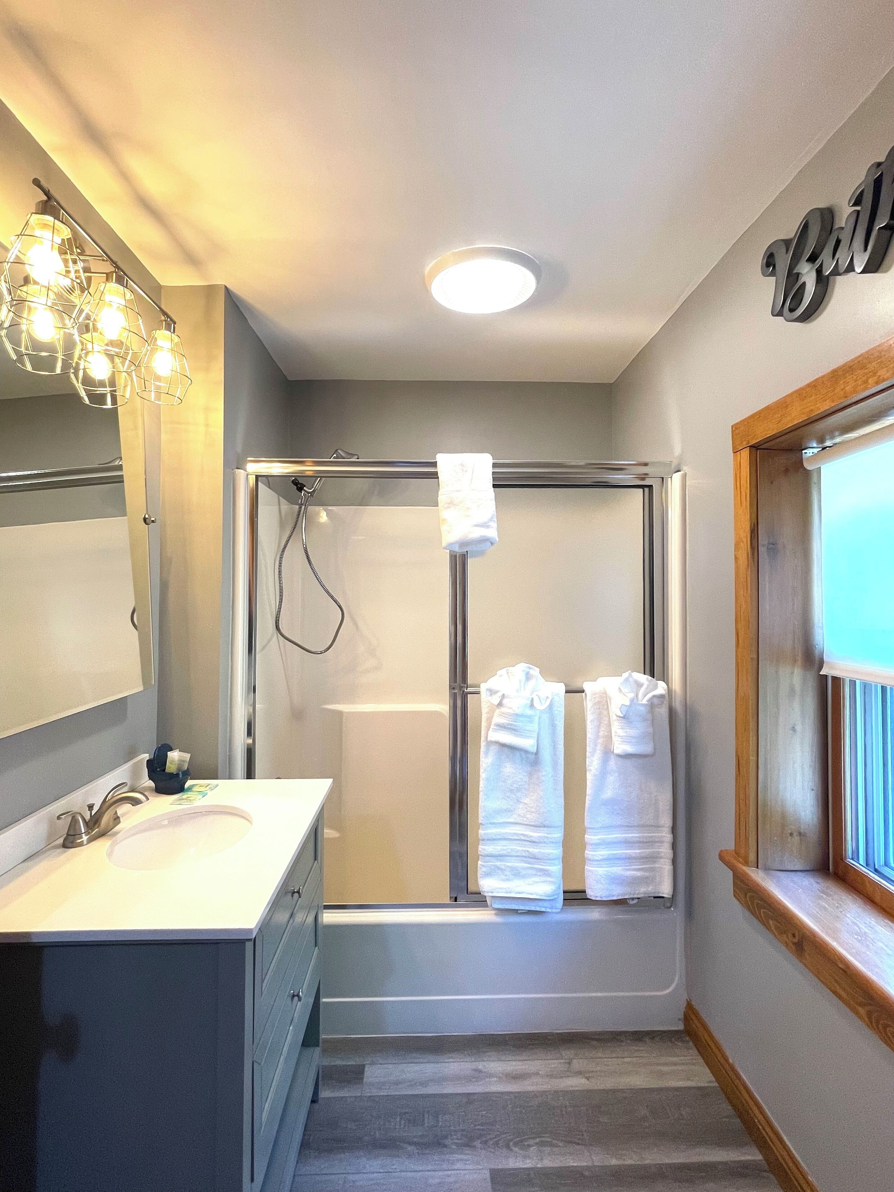 A modern bathroom with a glass shower enclosure, a vanity with a sink, and a towel rack with two towels.