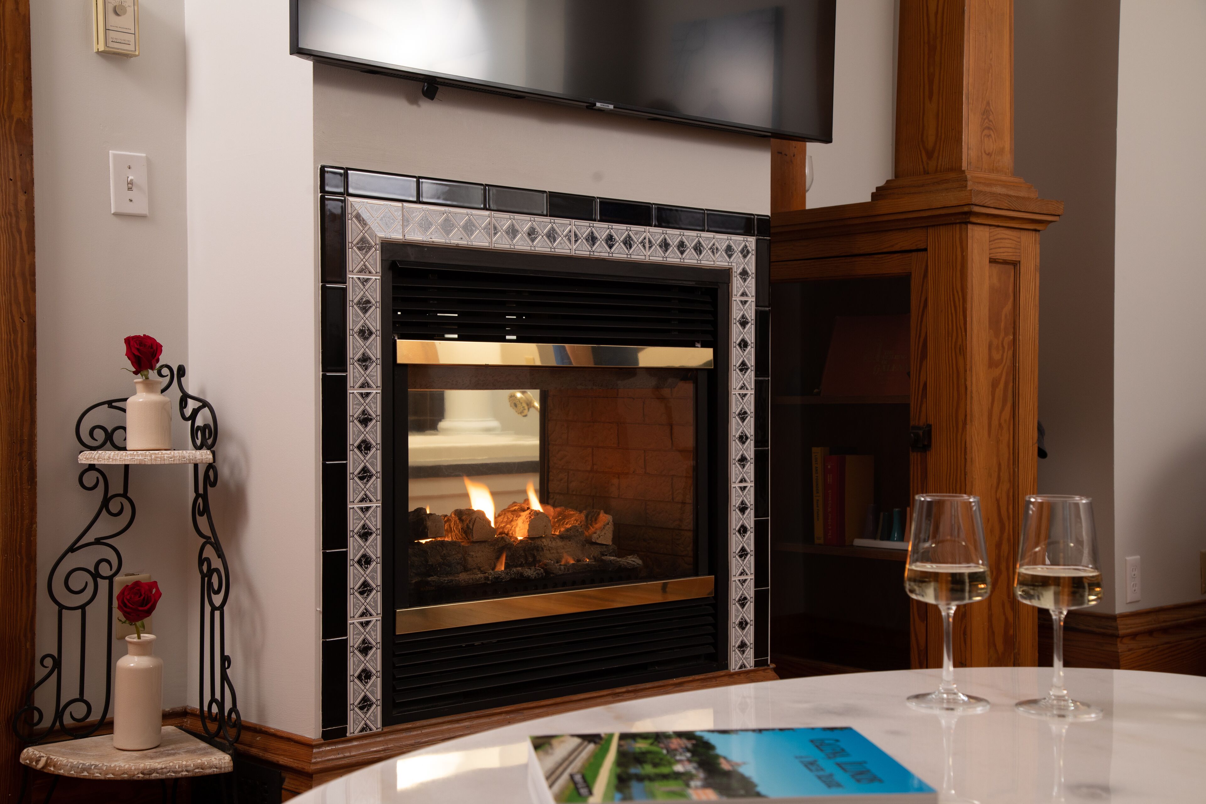 A fireplace with a tiled surround, a mounted television above it, and two glasses of wine on a table in front.