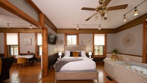 A spacious bedroom with a large bed, a sitting area with a desk, and a separate bathroom with a bathtub. - Hotel Galena (Galena)