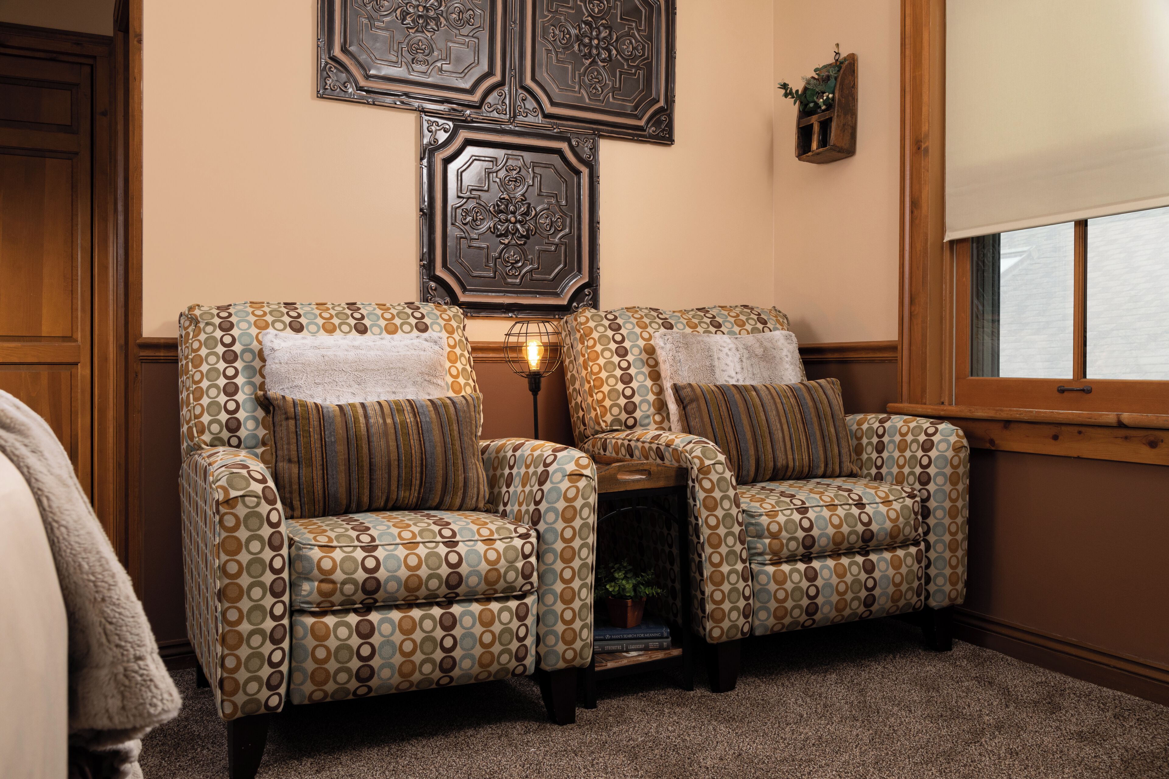 A cozy room with two patterned armchairs, a small table with a lamp, and decorative wall art.