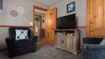 Een woonkamer met twee fauteuils, een houten tv-meubel met een flatscreen en decoratieve wandkunst.