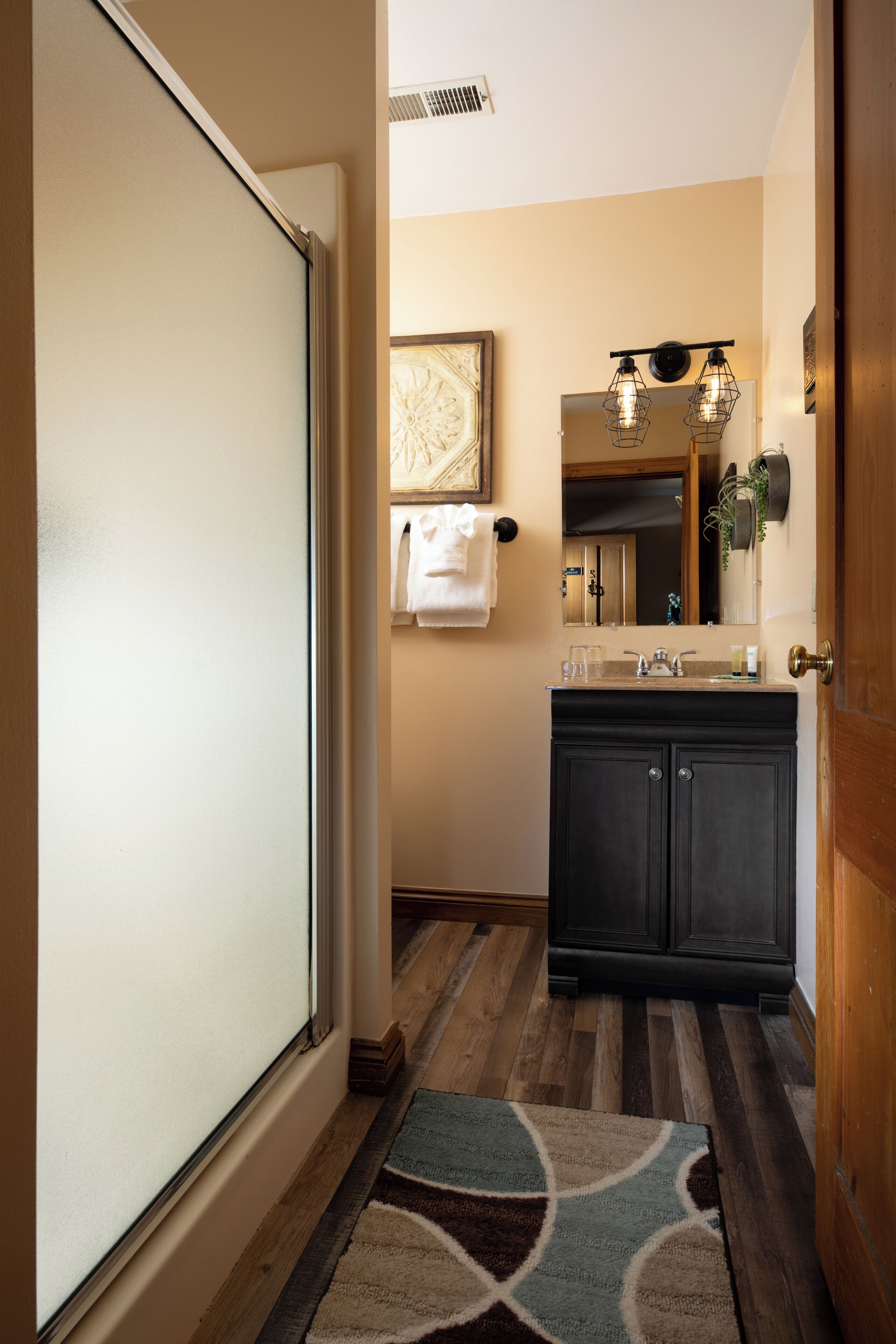 A bathroom with a wooden floor, a sink with a mirror, and a towel hanging on the wall.