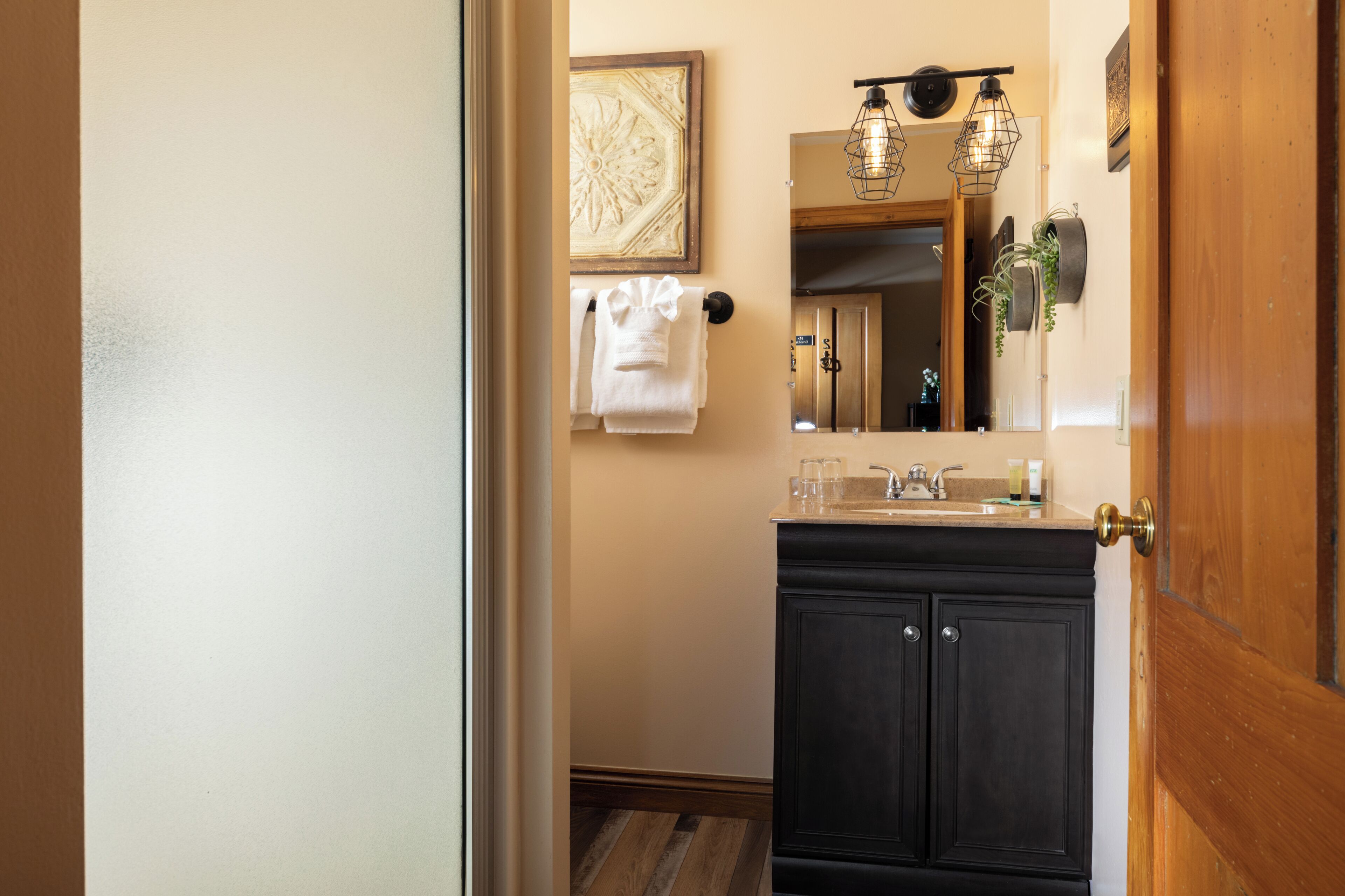 A bathroom with a wooden door, a dark cabinet, a sink, and a mirror.