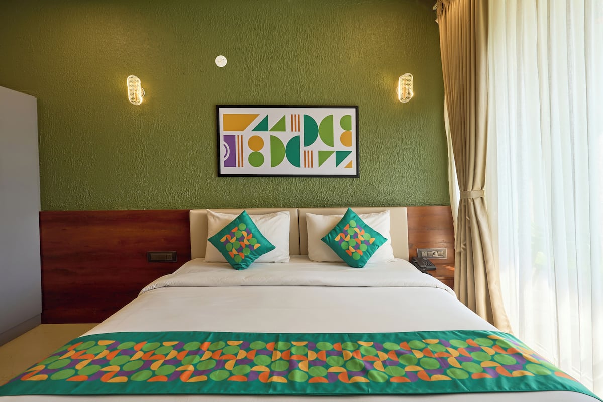 Una habitación de hotel con una cama, dos almohadas, una pared verde y una obra de arte enmarcada.