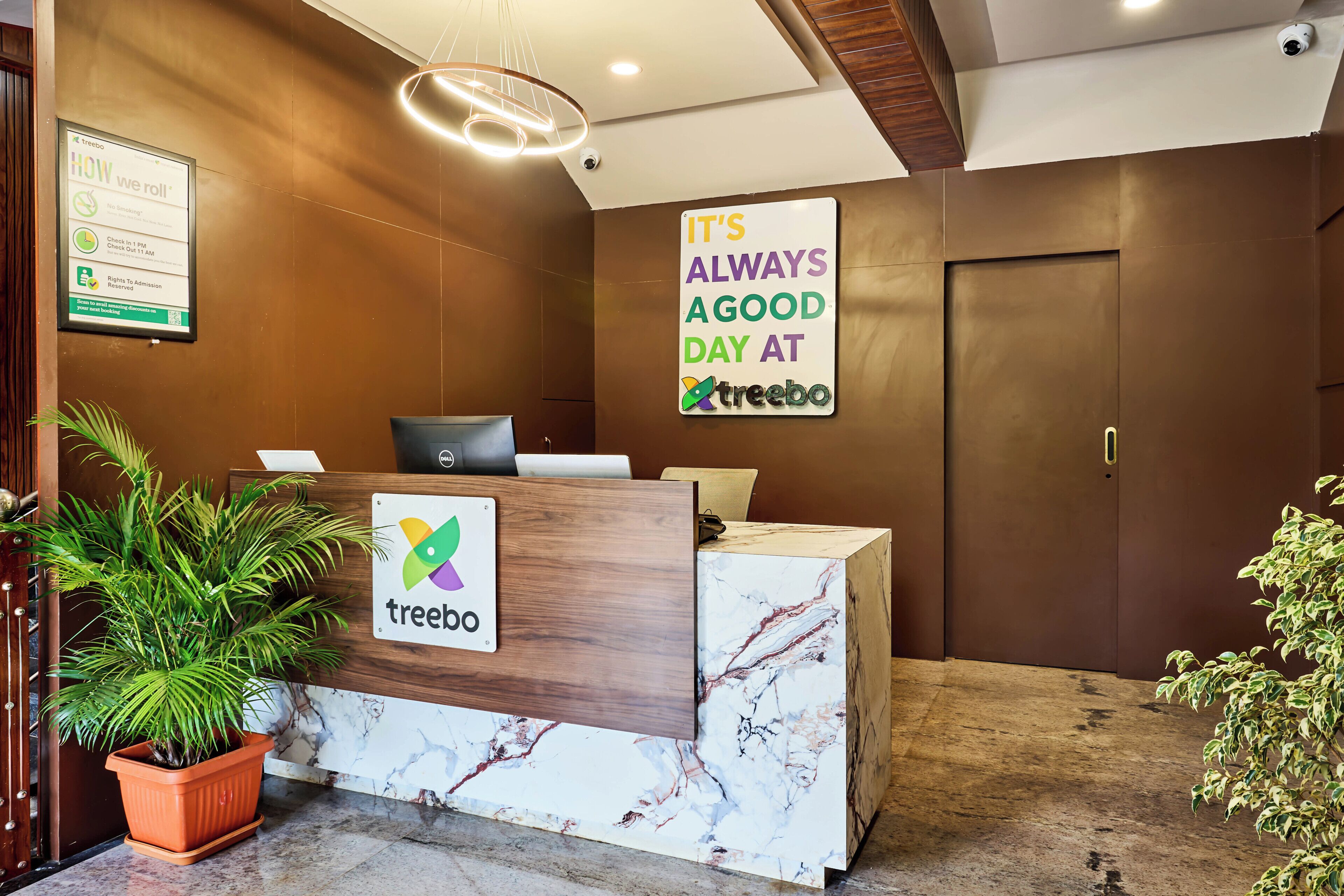 En receptionsdisk med et 'treebo'-skilt, en potteplante og et skilt, der siger 'Det er altid en god dag på treebo'.
