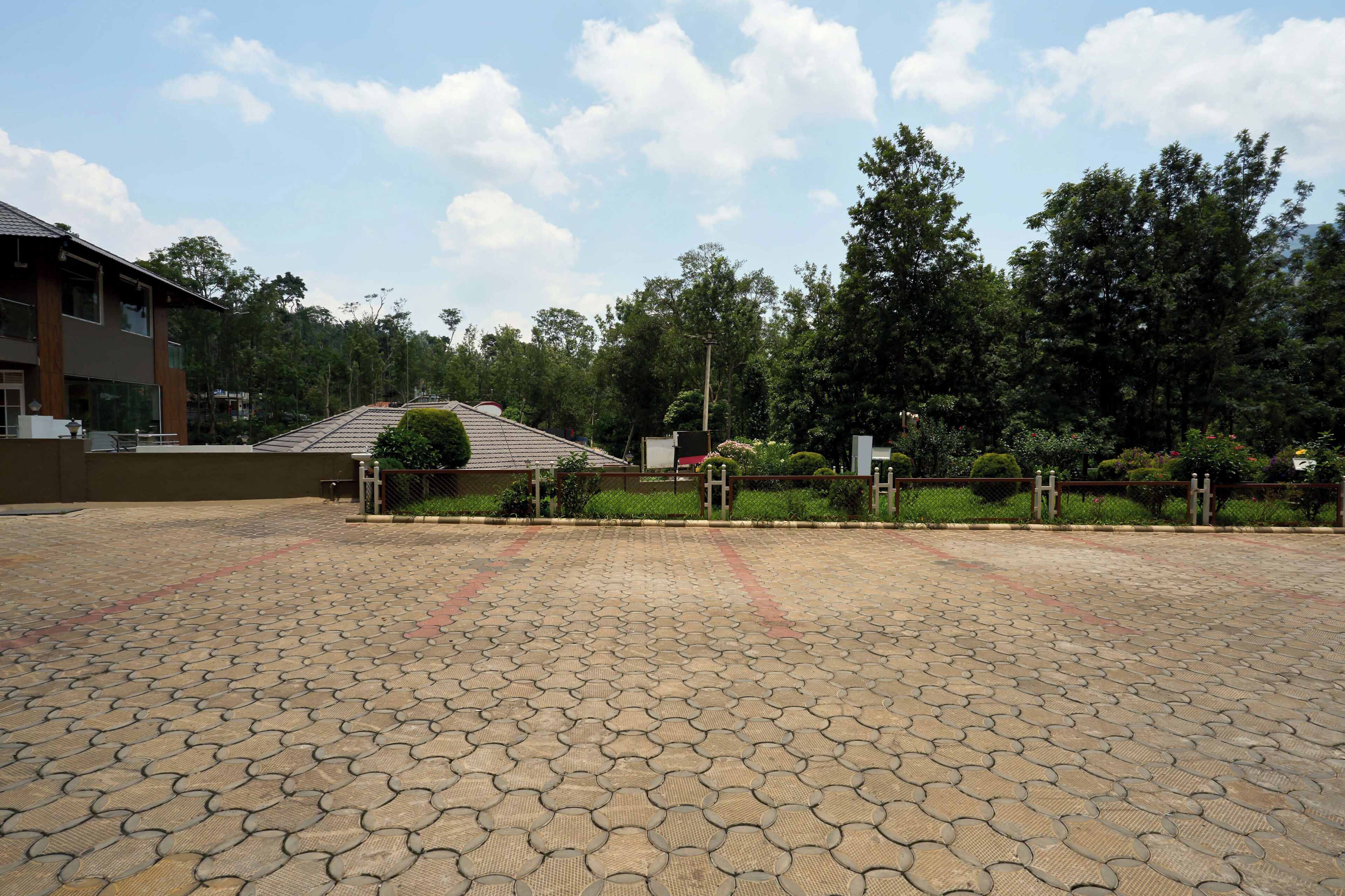 A paved courtyard with a building in the background, surrounded by trees and greenery.
