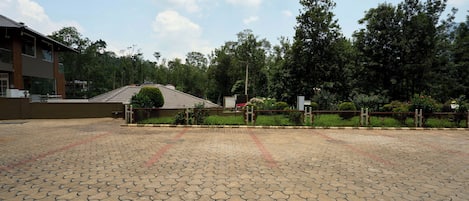 A paved courtyard with a building in the background, surrounded by trees and greenery.