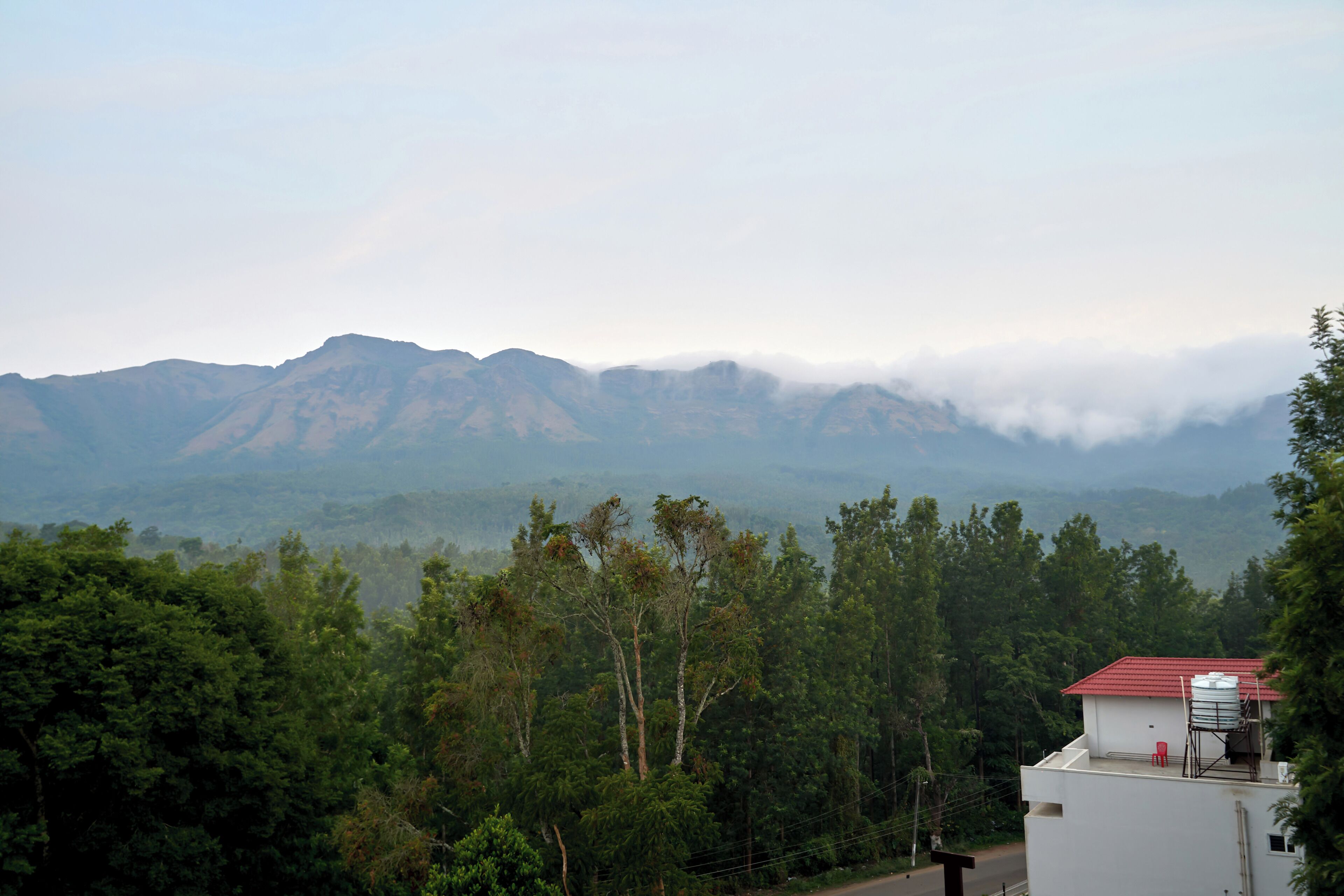 A building with a red roof, surrounded by dense green trees and mountains in the background.