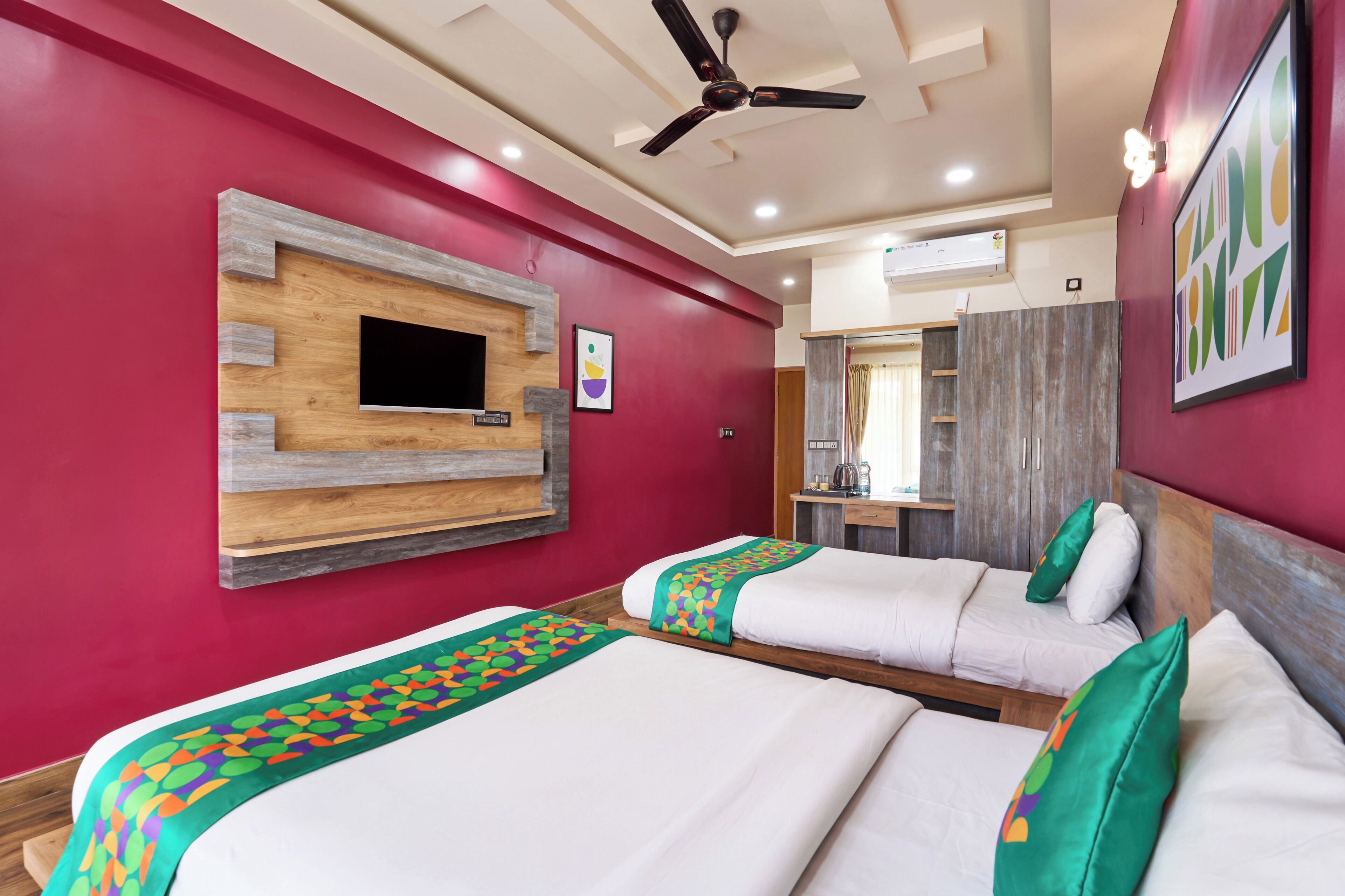 Habitación de hotel con dos camas, ventilador de techo, televisión montada y una pared decorativa de madera.