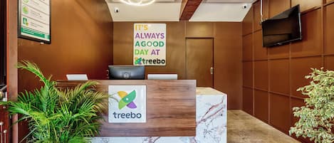 A reception desk with a sign that says 'It's always a good day at treebo,' a reception area with a potted plant, a desk, and a flat-screen TV mounted on the wall.