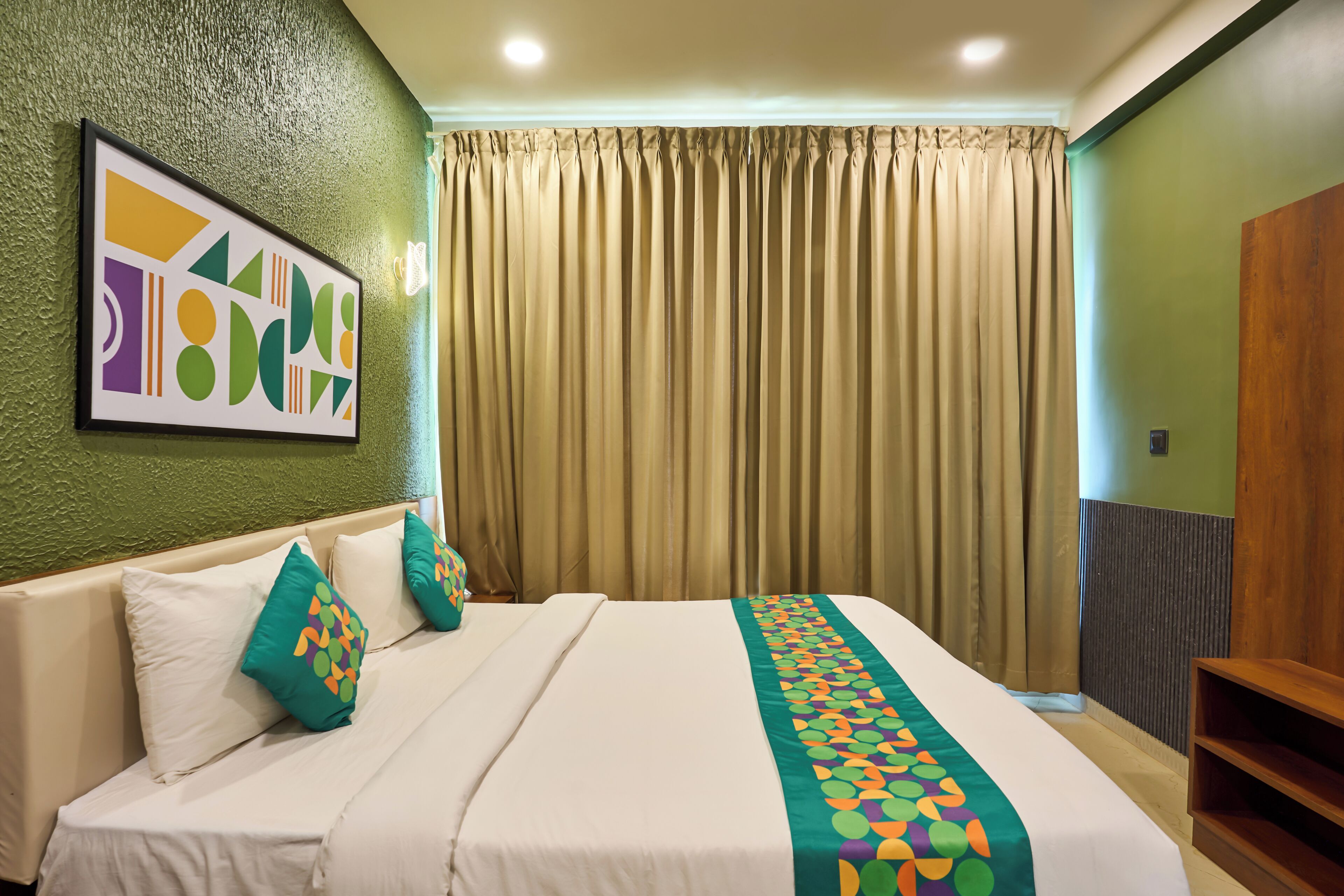 A hotel room with a bed, a green textured wall, a framed abstract art piece, and a curtain.