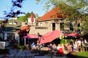 An outdoor dining area with red umbrellas, a building with a sign reading 'Sorrento's', and a bar named 'BARRA Sports Club' in the background. - The Elk Suite in Downtown Banner Elk (Banner Elk)