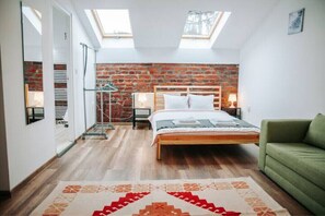 Une chambre avec un puits de lumière, un mur en briques, un lit en bois, un canapé vert et un tapis à motifs.