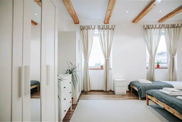 Un dormitorio moderno con dos camas, vigas de madera, paredes blancas y ventanas grandes con cortinas.
