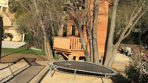A wooden playhouse with a trampoline in a backyard.