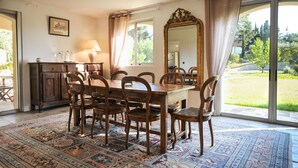 A dining room with a wooden table and chairs, a mirror, and a view of a garden through large windows.