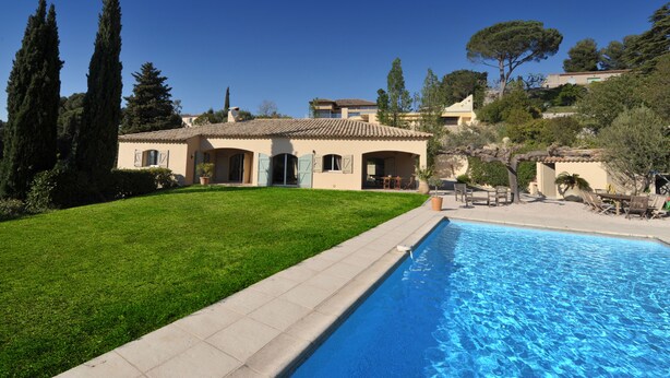 A Mediterranean-style villa with a swimming pool, a well-maintained lawn, and a view of surrounding hills.