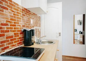 Compact kitchen area with a brick backsplash and modern countertop, featuring a stainless steel sink and white cabinet.