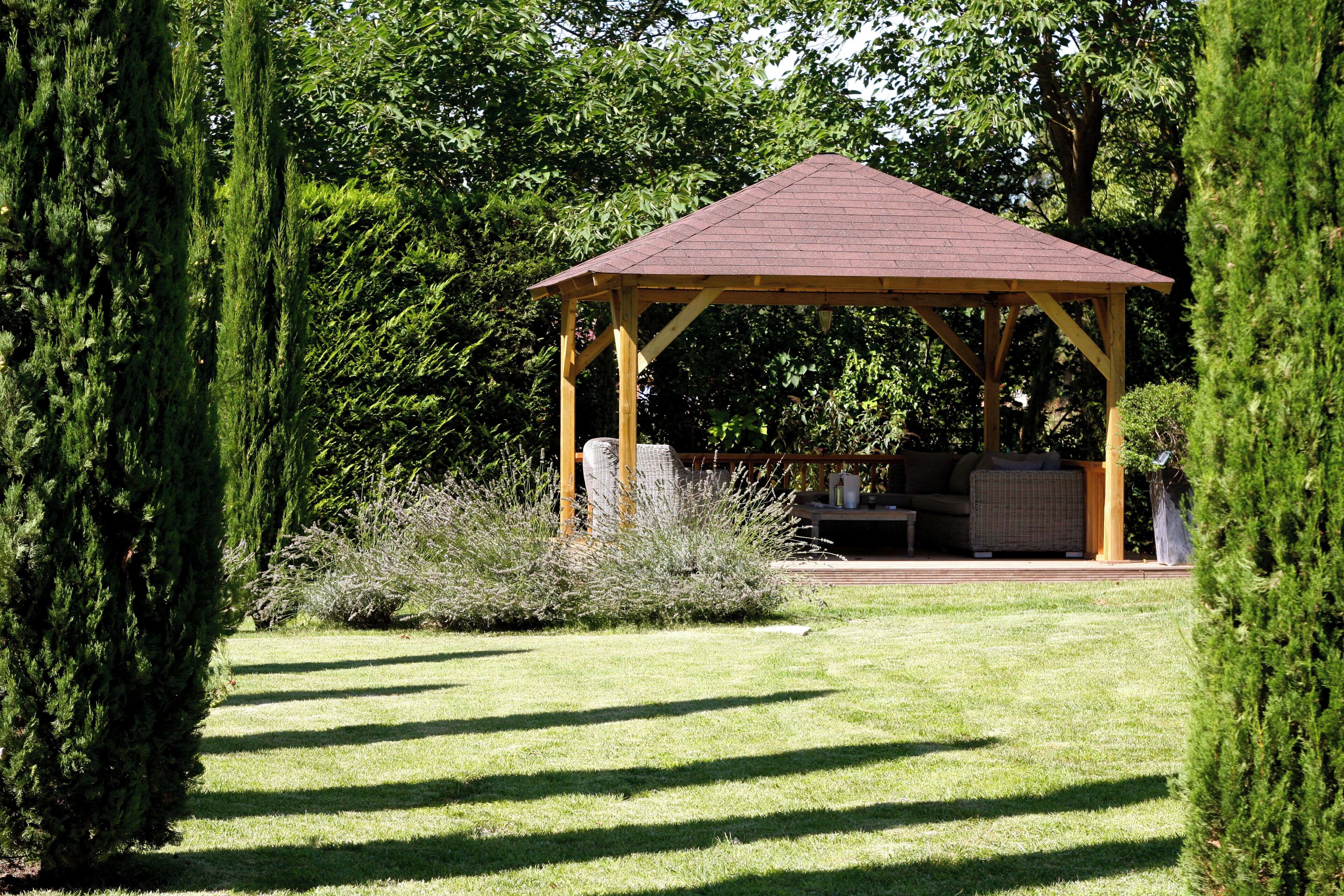 A gazebo with a wooden structure and a red roof, surrounded by a well-maintained lawn and various shrubs.
