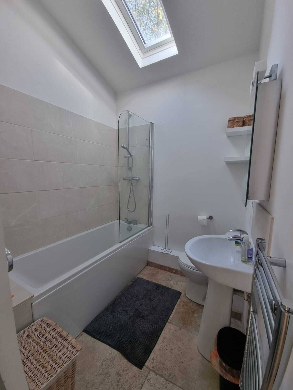 Een moderne badkamer met een dakraam, een badkuip, een douche en een wastafel.