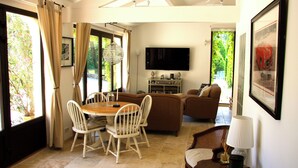 Un coin repas avec une table et des chaises, un canapé, un téléviseur fixé au mur et une fenêtre avec des rideaux.