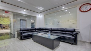 Una zona de recepción con un sofá de cuero negro, una mesa de centro de vidrio y un reloj en la pared.
